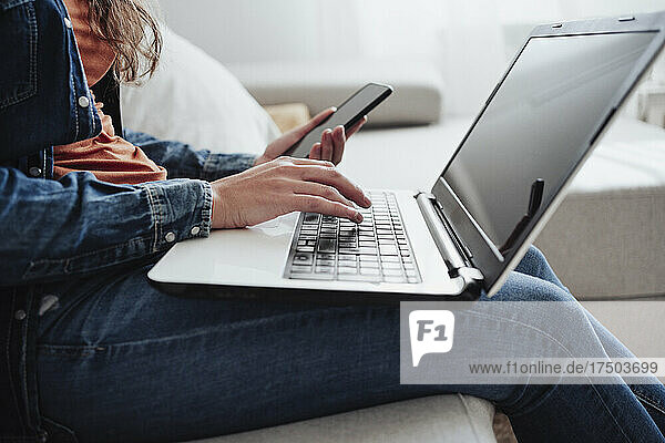 Woman with mobile phone using laptop in living room