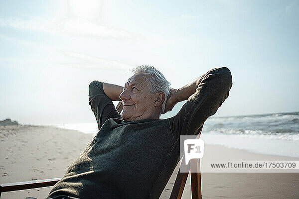 Smiling senior man with hands behind head relaxing at beach