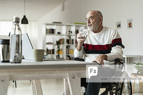 Senior businessman with drinking glass looking at laptop on table