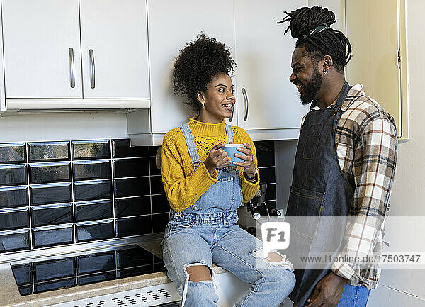 Lächelnde Frau mit Becher im Gespräch mit ihrem Freund an der Küchentheke