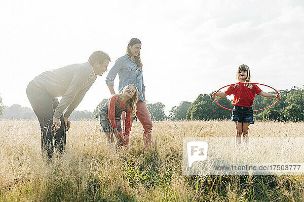 Eltern und Schwester schauen sich ein Mädchen an  das im Park mit Hula Hoop spielt