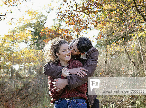 Young man kissing girlfriend in autumn forest