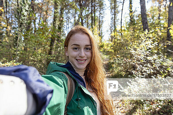 Smiling redhead young woman hiking in forest