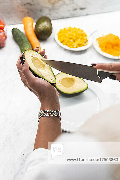 Woman slicing avocado with kitchen knife at home