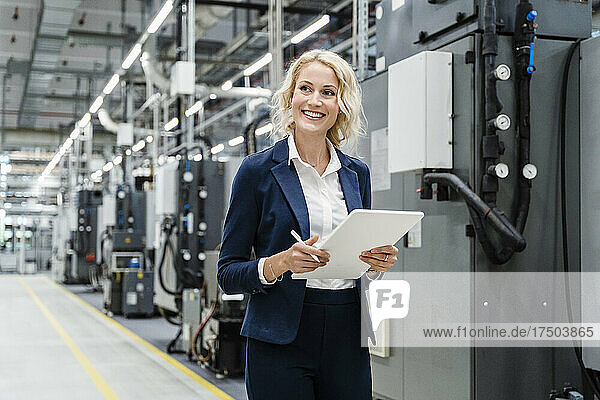 Smiling businesswoman with tablet PC at industrial equipment