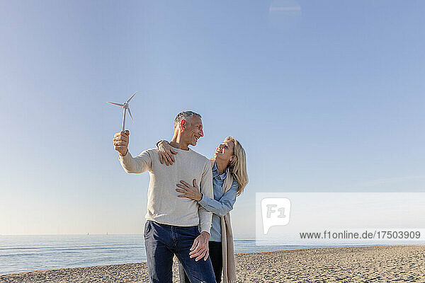 Mann hält Windturbinenmodell und blickt Frau am Strand an