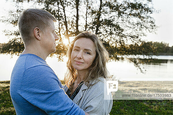 Man embracing blond woman in park at sunset