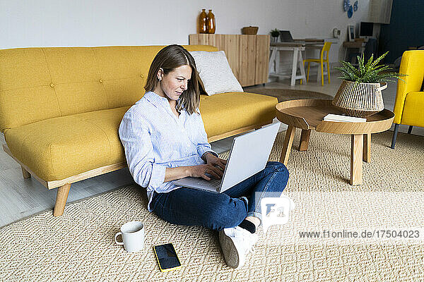 Woman using laptop sitting on carpet at home