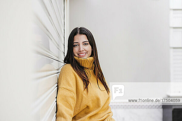 Smiling woman leaning on white wall