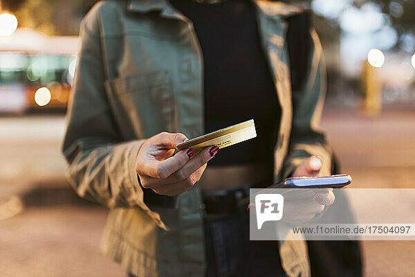 Frau mit Kreditkarte tätigt nachts Online-Einkäufe per Mobiltelefon