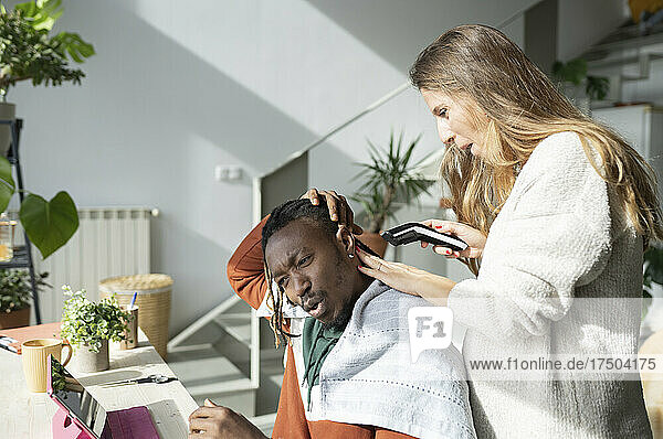 Pregnant woman with hair clipper cutting hair of man at home