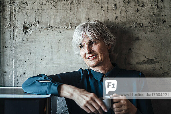 Smiling businesswoman with coffee cup in front of wall