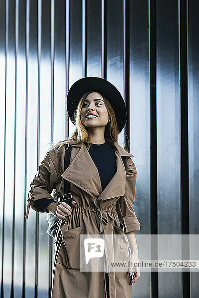 Smiling woman wearing hat and trenchcoat in front of wall