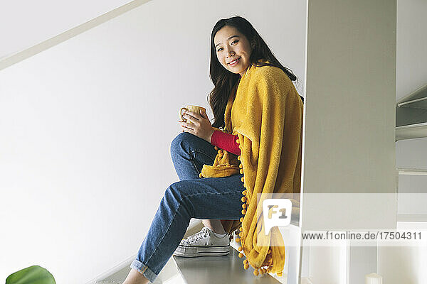 Lächelnde Frau mit Decke und Kaffeetasse auf Stufen