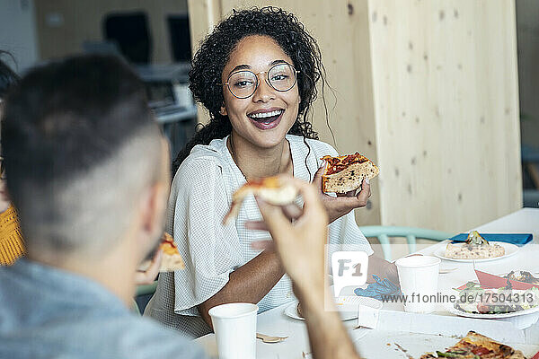 Happy woman with pizza looking at colleague in lunch break