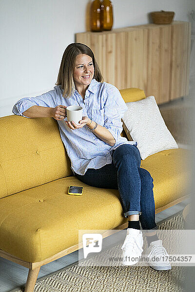 Smiling woman with coffee cup on sofa at home