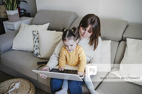 Mother using laptop with daughter on sofa