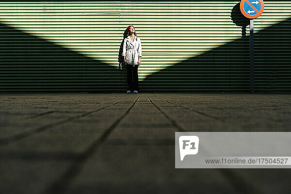 Woman standing on footpath in front of corrugated wall