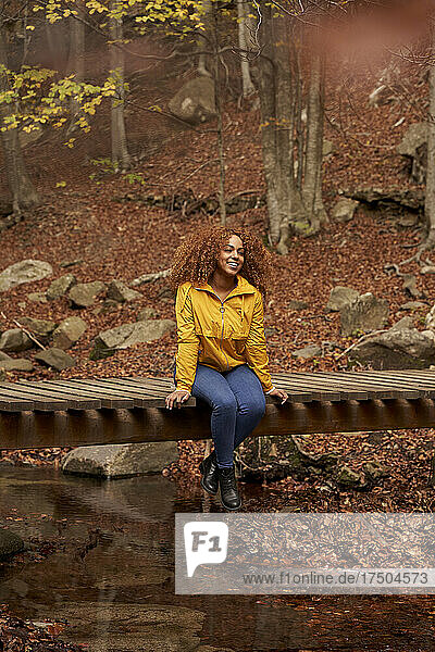 Smiling woman sitting on bridge in autumn forest
