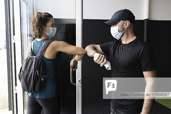 Freunde mit schützender Gesichtsmaske grüßen im Fitnessstudio