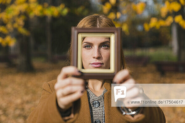 Junge Frau schaut durch Fotorahmen im Herbstpark