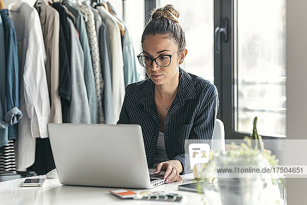 Junger Modedesigner mit Laptop am Schreibtisch