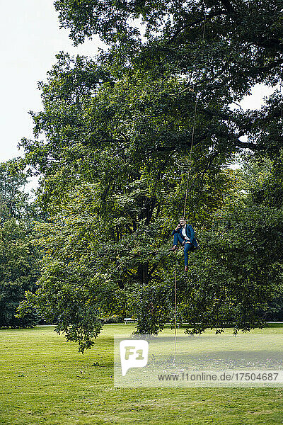 Businessman sitting on tree branch with rope at park