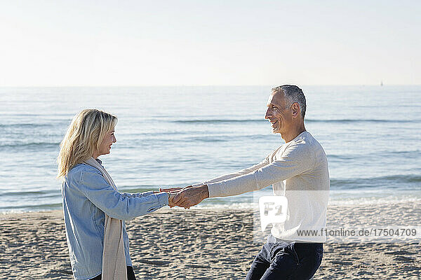 Verspieltes Paar hält Händchen am Strand