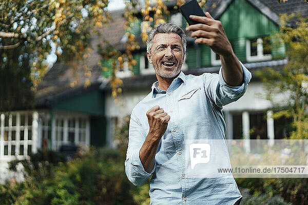 Glücklicher Mann jubelt und macht ein Selfie mit dem Smartphone im Hinterhof