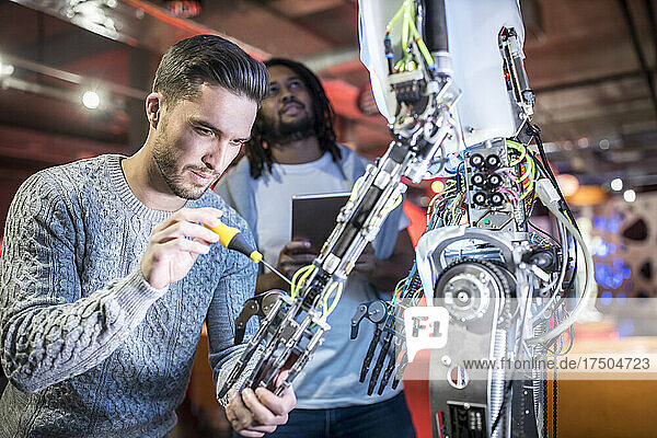 Engineer fixing robotic arm with colleague holding tablet PC at workshop