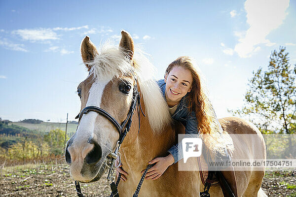 Lächelnde Frau sitzt am Wochenende auf einem Pferd auf der Wiese