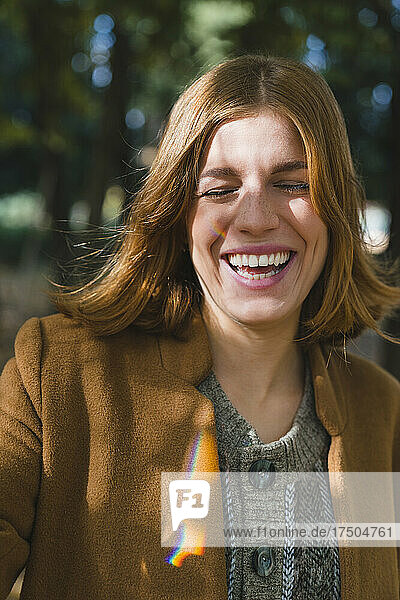 Young woman with eyes closed laughing in autumn park
