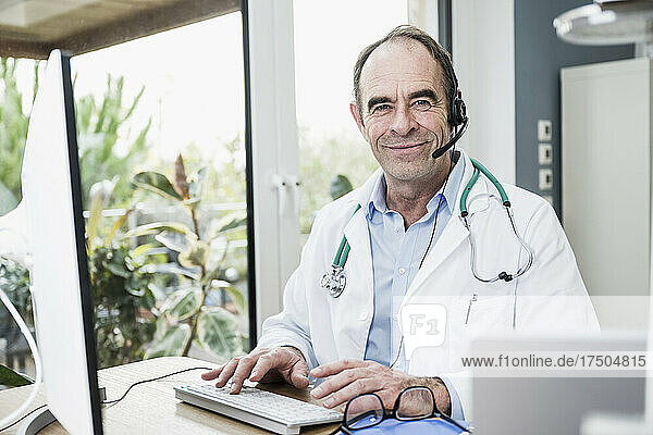 Smiling doctor wearing headset sitting at clinic