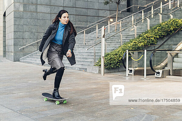 Businesswoman skateboarding by office building