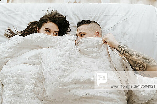 Couple under duvet looking at each other on bed