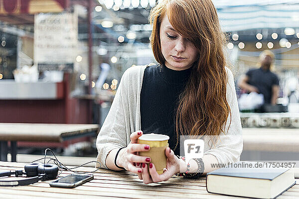 Redhead woman holding disposable coffee cup at cafe