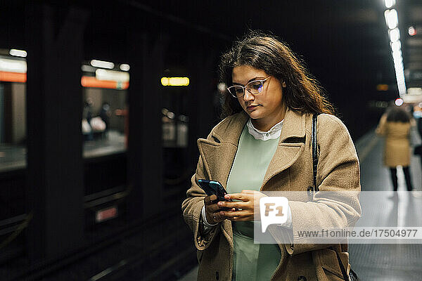 Young female commuter using mobile phone at railroad station platform