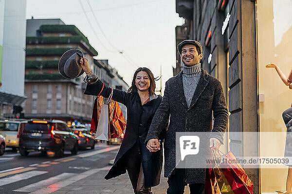 Happy girlfriend and boyfriend holding hands while walking together in city