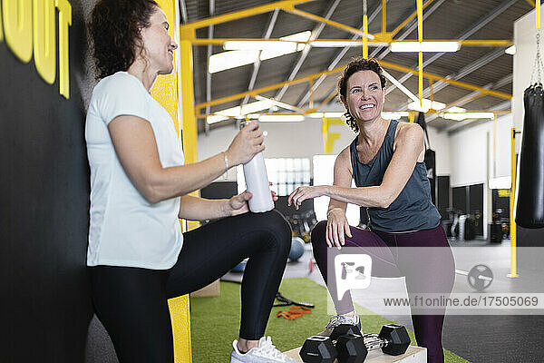 Sportswoman with water bottle looking at friend in gym