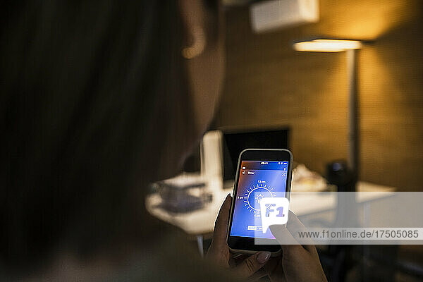 Woman using mobile phone with light bulb icon on screen at home