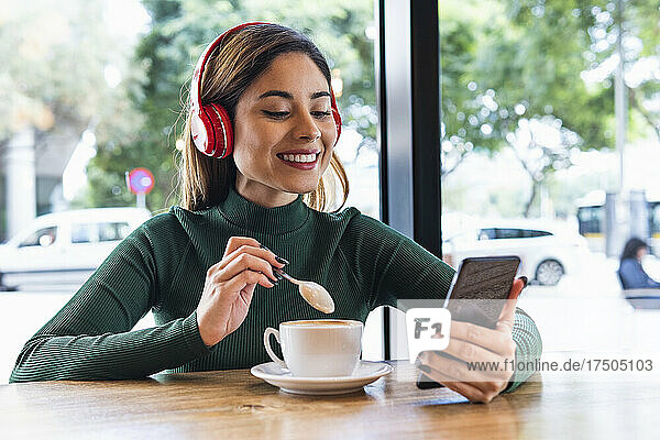 Smiling woman with wireless headphones using mobile phone in cafe