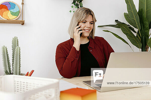 Smiling businesswoman talking on smart phone working on laptop
