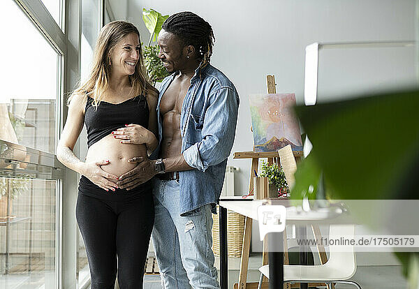Happy man touching belly of smiling pregnant woman at home