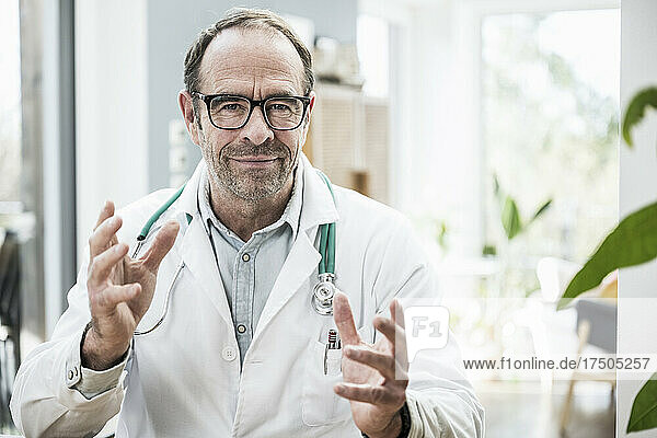 Smiling doctor wearing eyeglasses gesturing in clinic