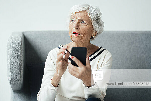 Nachdenkliche ältere Frau mit Smartphone zu Hause