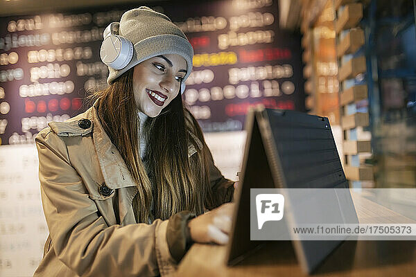Woman with headphones using touch screen laptop at cafe