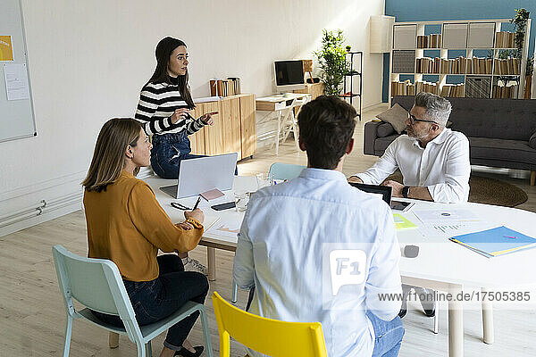 Young businesswoman discussing with colleagues sitting on desk at office