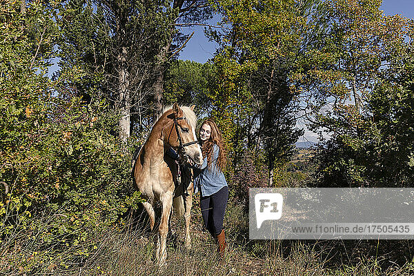 Young woman with horse walking in meadow on sunny day during weekend