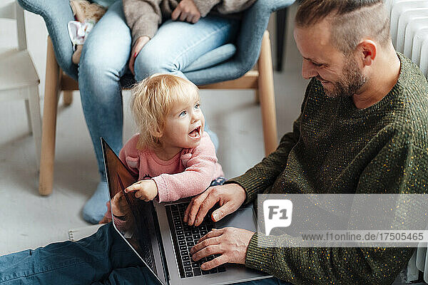 Tochter zeigt auf Laptop auf Vaters Schoß  Mutter im Hintergrund