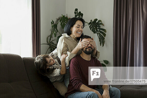 Playful girl holding mother's hand covering eyes of father at home